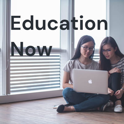two teens looking at a laptop together while sitting on the floor with text Education Now