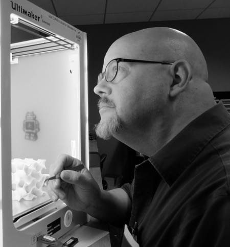 George Wiman looking intently into a 3D printer while holding a pair of tweezers